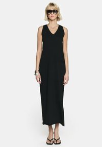Czarna, bezrękawnikowa sukienka maxi z dekoltem w serek. Gładki materiał, prosty krój, w połączeniu z czarnymi sandałami i dużymi okularami przeciwsłonecznymi.