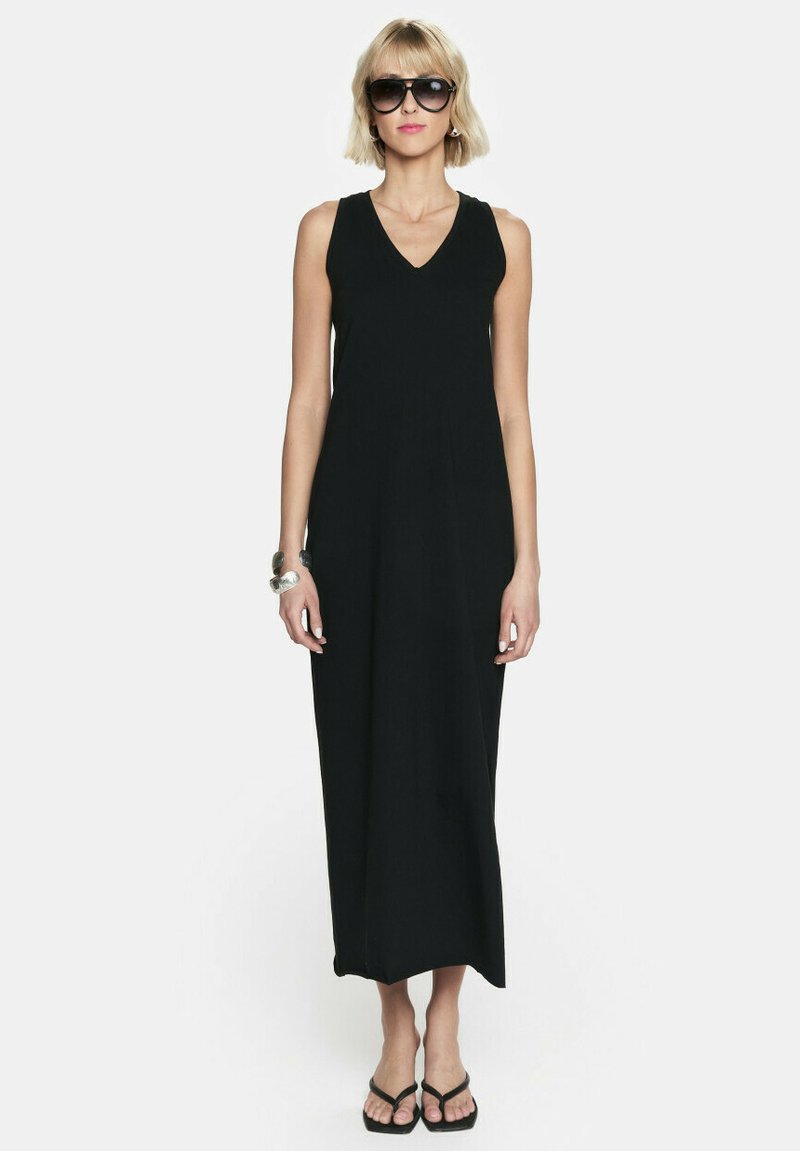 Czarna, bezrękawnikowa sukienka maxi z dekoltem w serek. Gładki materiał, prosty krój, w połączeniu z czarnymi sandałami i dużymi okularami przeciwsłonecznymi.