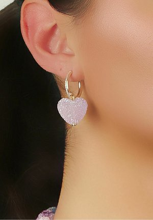 Guldtonade hoopsmycken med en lila hjärtformad charm i resin med texturerad yta och en liten beaddetalj.