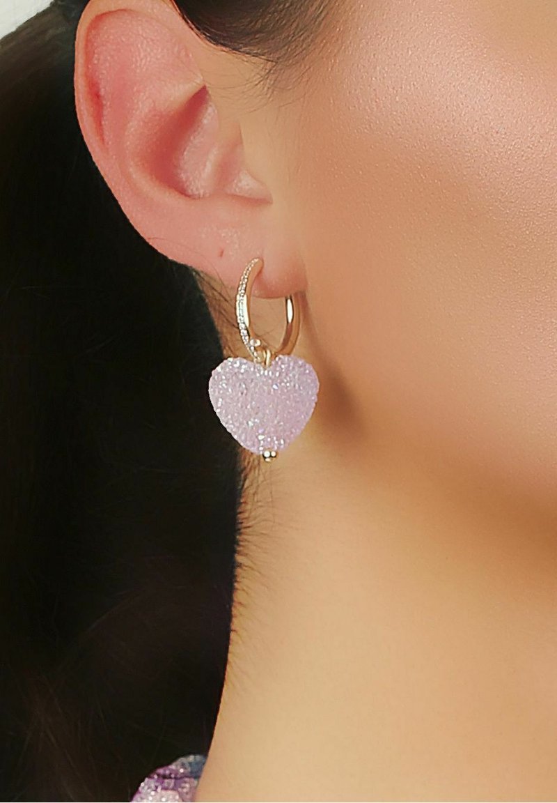 Guldtonade hoopsmycken med en lila hjärtformad charm i resin med texturerad yta och en liten beaddetalj.