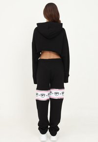 Svart kort hoodie med huva, tillsammans med svarta sweatpants med en djärv rosa och vit remsa med ögonmönster och grafiska accenter.