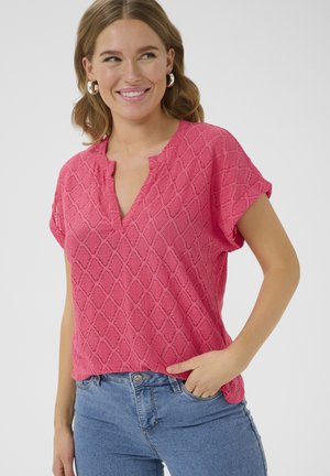 Korte mouwen roze top met een gestructureerd ruitpatroon, voorzien van een v-hals en opgerolde mouwen. Gecombineerd met lichtblauwe jeans.