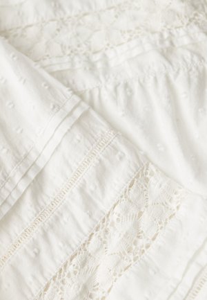 Tela blanca con pequeños puntos texturizados, inserciones de encaje y pliegues pintuck que crean un patrón textil delicado e intrincado.