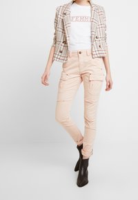 Sako s kostkovaným vzorem v béžové, krémové a cihlové barvě; bílý tričko s potiskem "FEMME"; světle růžové cargo kalhoty; černé kotníkové boty.