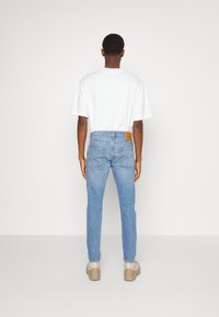 Vaaleansiniset slim fit -farkut haalistuneella tekstuurilla, takataskuilla ja ruskealla nahkaisella merkintätarralla vyötäröllä. Yhdistetty valkoiseen lyhythihaiseen paitaan.