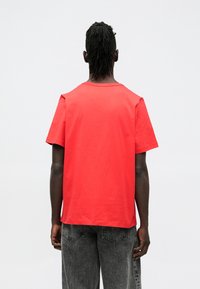 Czerwona bawełniana koszulka z okrągłym dekoltem i krótkimi rękawami, o prostym wzorze i luźnym kroju, zestawiona z szarymi spodniami dżinsowymi.