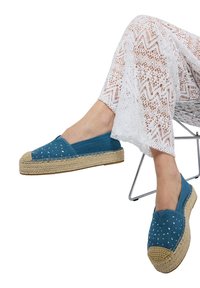 Espadrillas in tela blu con borchie bianche decorative, suola in juta intrecciata e punta rotonda, abbinate a pantaloni bianchi in pizzo.