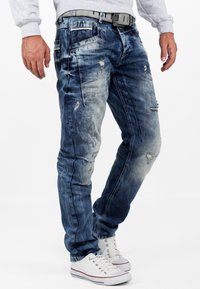 Jeans in denim blu sbiaditi con dettagli trasandati, cinque tasche e una vestibilità slim. Abbinati a sneakers in tela bianche e a una felpa grigia.