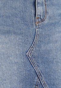 Tissu en denim bleu avec une couture en zigzag et des coutures marron contrastantes. La texture est lisse avec une apparence classique de délavage clair.
