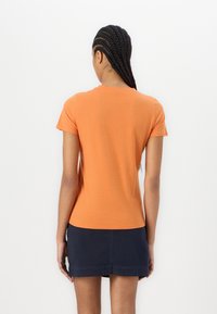 Short-sleeve orange t-shirt with a round neckline, paired with a dark blue skirt. The fabric appears smooth, with a fitted design.