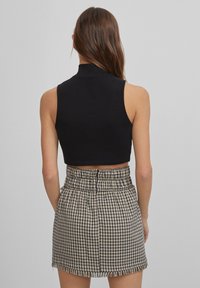 Czarny bezrękawnik w formie topu, zestawiony z wysokim mini spódnicą w kratkę, z postrzępionym dołem i marszczonym paskiem w talii.