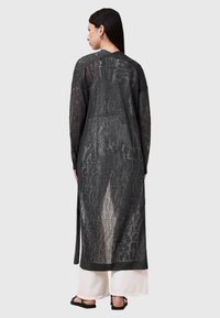 Lång svart cardigan i ett strukturerat, halvgennomsynligt material. Har rak skärning, långa ärmar och sidofickor för ökad rörlighet.