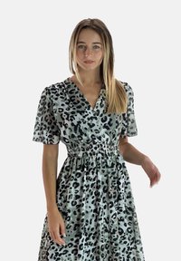 Blommig omslagklänning i ljusgrön med svart leopardmönster. Har korta puffärmar och en smockad midja för en luftig silhuett.