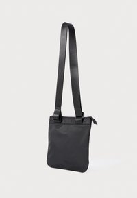 Borsa a tracolla rettangolare nera con tracolla regolabile e chiusura a zip appesa su uno sfondo chiaro e uniforme.