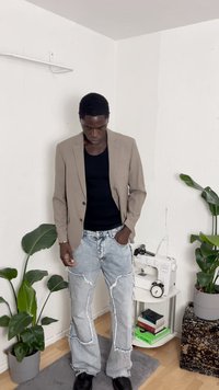 Blazer beige a medida sobre un top negro sin mangas, combinado con jeans desgastados de lavado claro y zapatos negros. Plantas de interior en el fondo.