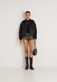 Μαύρο μπούφαν, εφαρμοστό μαύρο crop top, σορτς καμουφλάζ, μαύρες μπότες μέχρι το γόνατο και μια μικρή μαύρη τσάντα, όλα πάνω σε ουδέτερο φόντο.