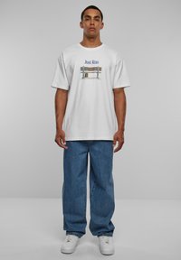 Hvid bomulds t-shirt med et grafisk print med teksten "Just Run" og et bænkdsg design. Båret med blå denim jeans og hvide sneakers.