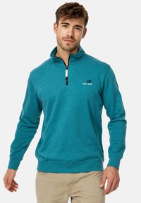 Sudadera de forro polar azul verdoso con cierre de cremallera, cuello alto, mangas largas y un pequeño logo bordado en el pecho.