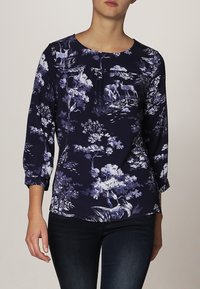 Blusa blu navy con maniche a tre quarti, caratterizzata da una stampa floreale e animale in tonalità di blu e bianco, con scollatura rotonda e pieghe.