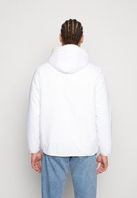 Giacca puffer bianca con cappuccio, dotata di un colletto morbido e testurizzato. Il materiale è liscio con una finitura leggermente lucida. Vestibilità casual.