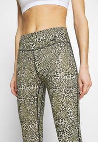 Leggings a vita alta con stampa leopardata, caratterizzati da tonalità di verde e nero, con una silhouette aderente e cuciture piatte.