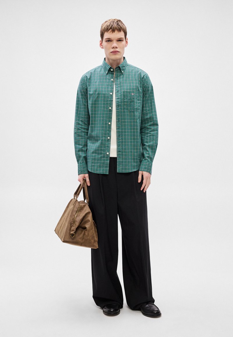 Green plaid shirt with button-down collar over a white shirt, paired with black wide-leg trousers and a brown leather bag.