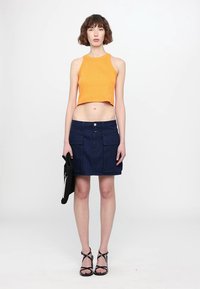 Oransje ribbet crop top og mørkeblå denimskjørt med frontlommer. Modellen holder en strukturert svart clutch. Svarte stroppelester fullfører antrekket.