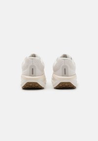Pantofi sport albi care prezintă o parte superioară din plasă respirabilă, un călcâi texturat moale și o talpă din cauciuc natural cu un model de tălpi geometric.