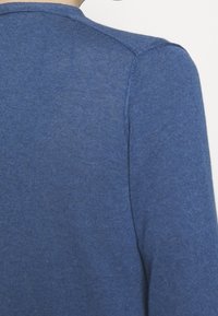 Modrý pletený svetr s hladkou texturou, s kulatým výstřihem a žebrovaným zdobením podél švů. Zadní část je převážně jednobarevná.