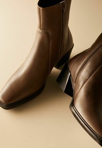 Bottines en cuir marron à bout pointu et texture lisse. Elles disposent d'une fermeture éclair sur le côté et d'un talon carré robuste.