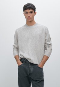 Light gray knit sweater with a crew neckline and ribbed cuffs, paired with dark gray jeans. The fabric appears soft and textured.