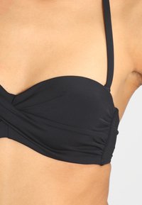 Černý bikiny top s twistovým předním designem, tenkými nastavitelnými ramínky a na bocích nařasenou texturou. Hladký povrch látky.