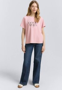 Ljusrosa kortärmad skjorta med texten "GOOD TIMES" i svart, matchad med mörkblå utsvängda jeans och vita sandaletter med klack.