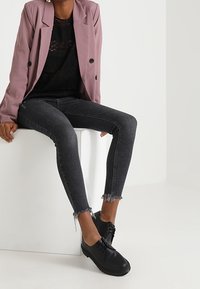 Mustat pitsitoppi, mauve bleiseri, tummanharmaat tiukat farkut, joissa on revitty helma, ja mustat nauhakengät. Minimalistinen muotoilu, jossa on sileät pinnat.