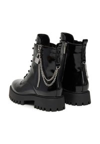 Stivali alla caviglia in pelle verniciata nera con suole spesse, dotati di cerniere laterali, catene decorative e un design con lacci frontali.