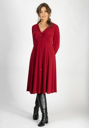 Red, long-sleeve dress with a V-neckline and button front. Flowy skirt and soft fabric, paired with black knee-high boots.