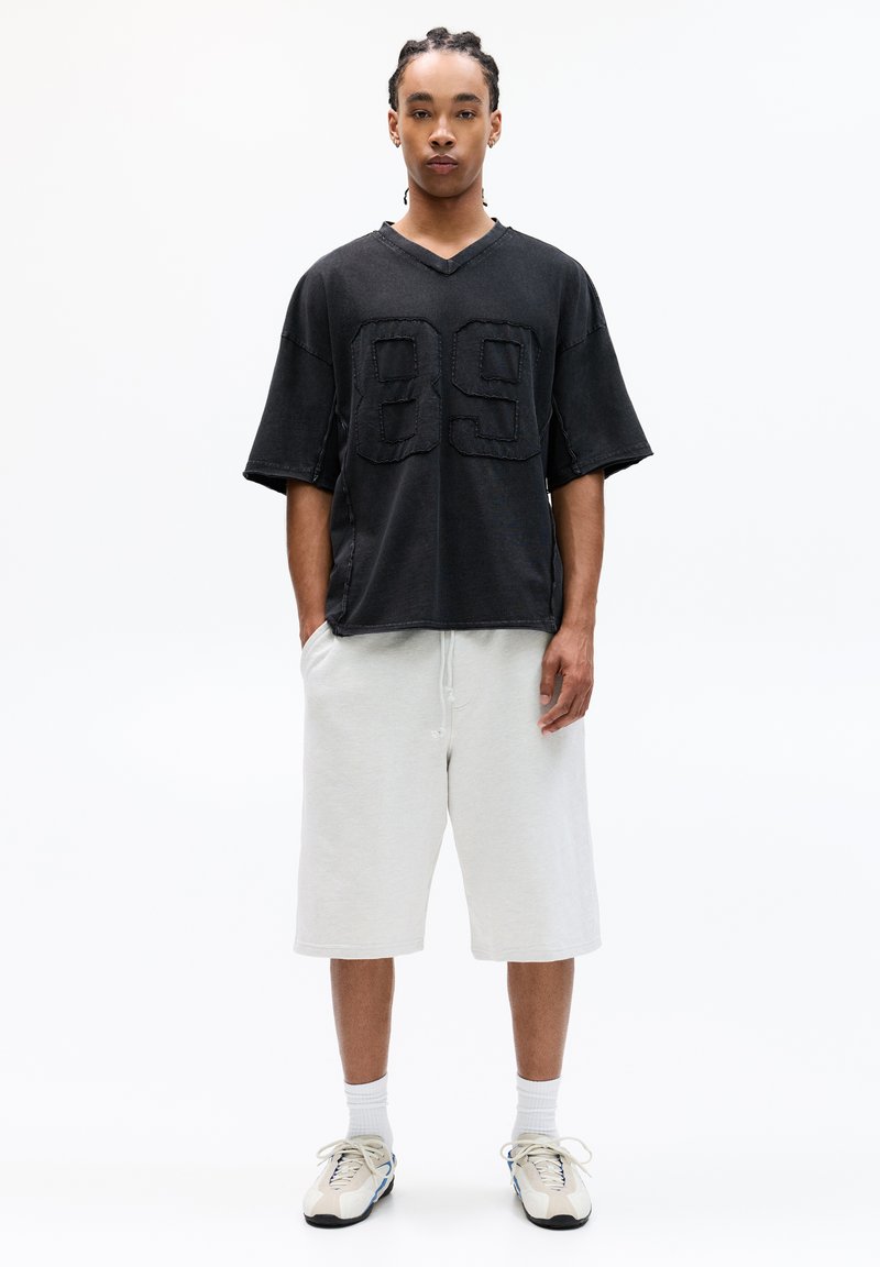 Sort oversized T-shirt med et "89" design, parret med lysegrå shorts. Stoffet ser blødt ud, og outfittet inkluderer atletiske sko.