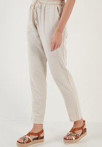 Beige, lichte, geweven broek met een elastische tailleband, verstelkoord en taps toelopende benen, getoond met een model dat espadrilles draagt.