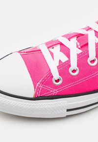 Baskets en toile rose avec lacets blancs, œillets argentés et embout en caoutchouc blanc. Dotées d'une bande noire le long de la semelle et d'un tissu texturé.