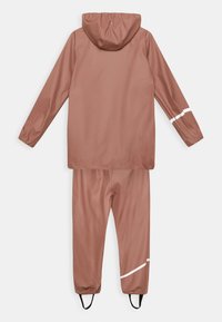 Ensemble deux pièces résistant à l'eau en rose poudré. Veste avec capuche et poignets élastiques ; pantalon avec accents réfléchissants blancs et sangles réglables aux chevilles.