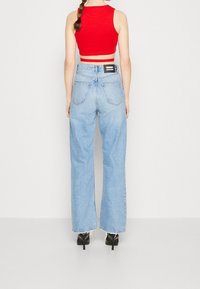 Jeans anchos de color azul claro con dobladillo sin terminar, combinados con una camiseta sin mangas roja. Presenta bolsillos traseros prominentes y una etiqueta negra en la cintura.