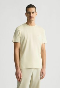 Helles Cremefarbene T-Shirt mit kurzarm, gefertigt aus weichem Stoff, mit klassischem Rundhalsausschnitt und dezentem Logo-Detail auf der Brust.