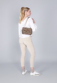 Béžové fitted kalhoty a bílé blouse spárované s vícebarevnou kabelkou se řetízkem a logem. Bílé tenisky se šedými akcenty.