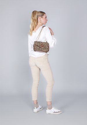 Pantaloni beige a sigaretta e una blusa bianca abbinati a una borsa multicolore con tracolla a catena e dettagli con logo. Sneakers bianche con accenti grigi.