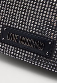 Borsa nera con una superficie testurizzata coperta di luccicanti borchie argentate. Presenta un'etichetta nera prominente con il testo "LOVE MOSCHINO."