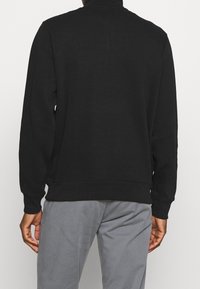 Felpa nera con maniche lunghe, polsini e orlo a costine, realizzata in un materiale morbido e strutturato, caratterizzata da un design con collo alto.