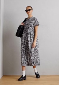 Šaty s čierno-sivým leopardím vzorom, po kolená, s krátkymi rukávmi, uvoľnený strih. Nosí sa s čiernymi robustnými loafers a textúrovanou čiernou kabelkou.