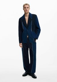 Denim-puku, jossa on sininen värimaailma, kontrastiväriset paneelit, lovettu kaulus ja valkoiset ommeltyöt. Yhdistetty tummiin kenkiin.