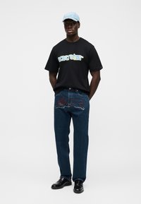 Μαύρο T-shirt με το σχέδιο "icecream", μπλε τζιν με κόκκινες και λευκές διακοσμήσεις, ανοιχτό μπλε καπέλο, μαύρα παπούτσια.