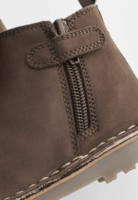 Stivale alla caviglia in pelle marrone con zip laterale, cuciture a contrasto e suola texturizzata. Finitura liscia con un design durevole.